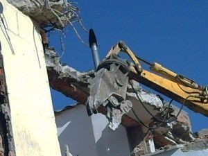 Una excavadora amarilla está demoliendo un edificio con un cielo azul de fondo.