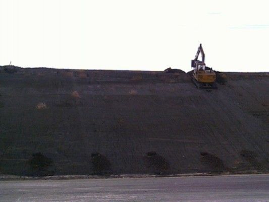 Una excavadora está parada en la cima de una colina al lado de una carretera.