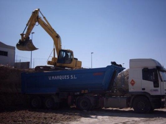 Una excavadora amarilla está cargando tierra en un camión volquete que dice varques sl