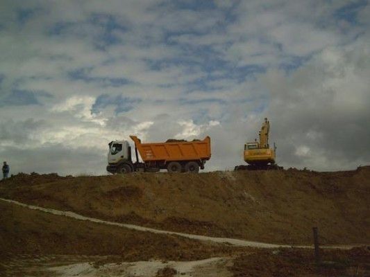 Un camión volquete está estacionado en la cima de una colina de tierra al lado de una excavadora.