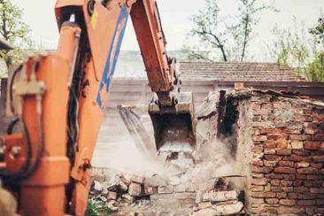 Una excavadora está demoliendo un edificio de ladrillos.