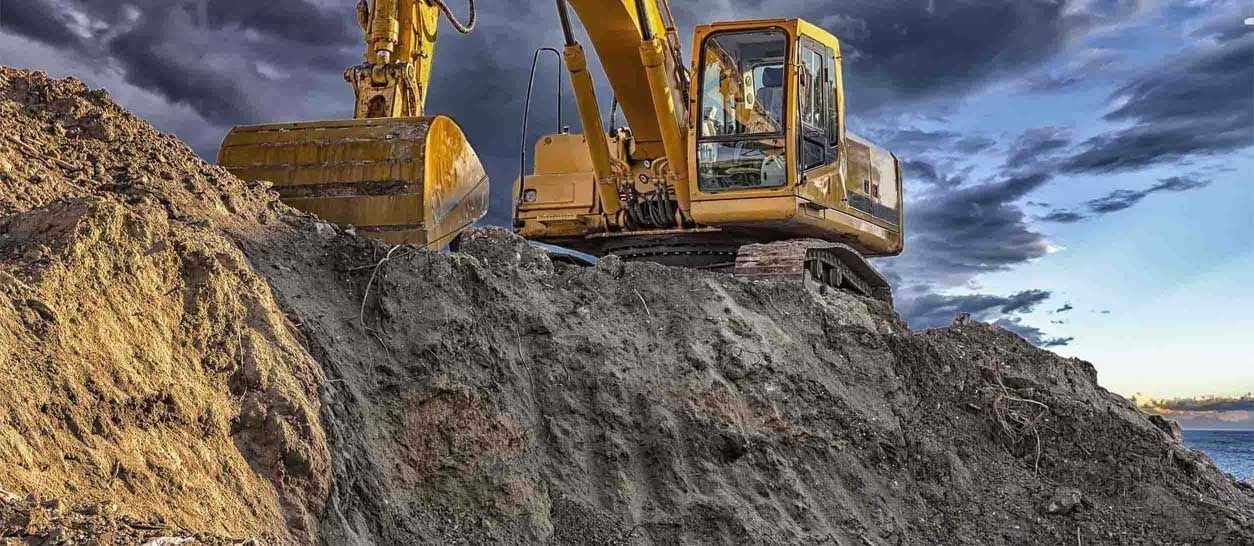 Una excavadora amarilla está sentada encima de una pila de tierra.