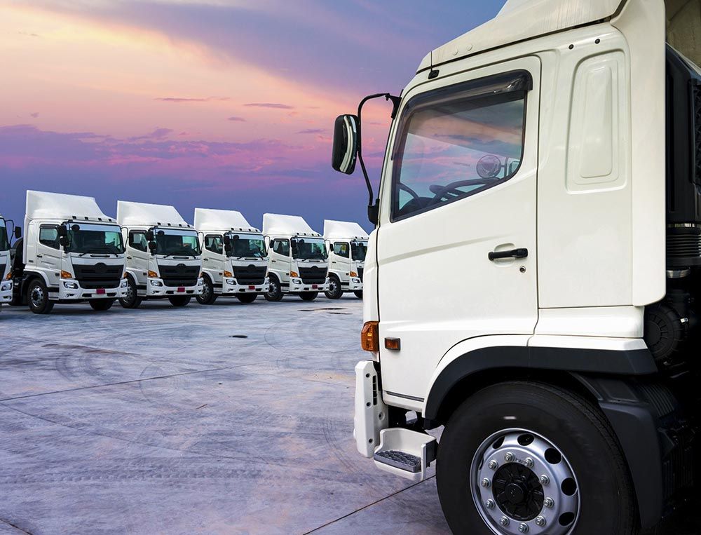 Camionetas de reparto blancas estacionadas en un aparcamiento al atardecer, con una de ellas en primer plano.