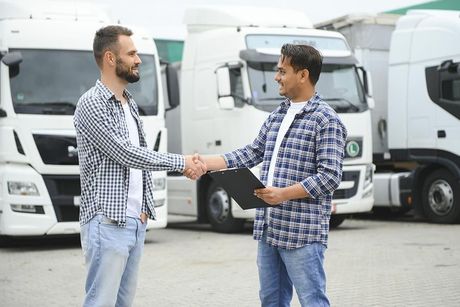 Dos hombres dándose la mano frente a camiones de reparto blancos estacionados.