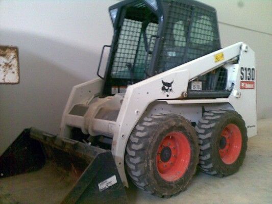 Minicargadora Bobcat blanca con pala en el interior, vista de lado.