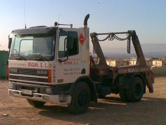 Grúa blanca estacionada en tierra, con brazo de grúa y letreros de una empresa española en el lateral.