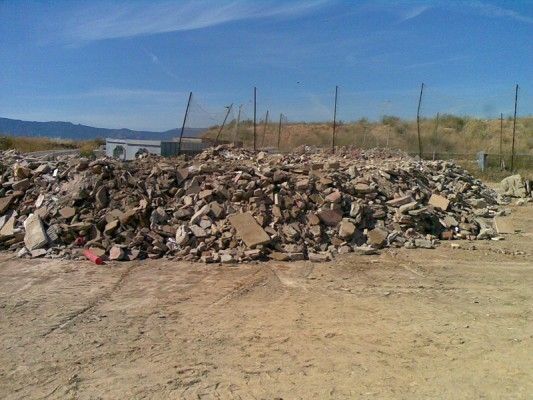 Gran montón de escombros y restos en una zona árida al aire libre bajo un cielo azul.