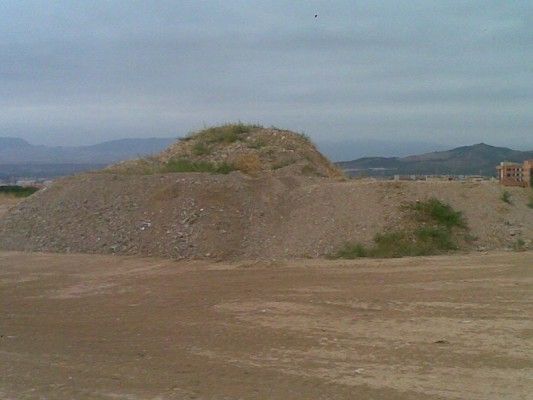 Un gran montículo de tierra y grava en una zona árida y despejada bajo un cielo nublado.