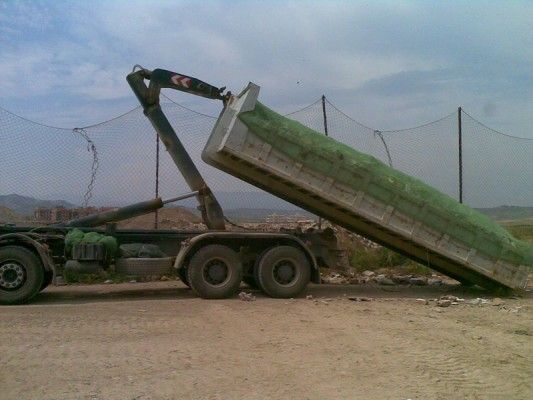 Camión volquete verde con plataforma elevada descargando tierra en una obra de construcción.