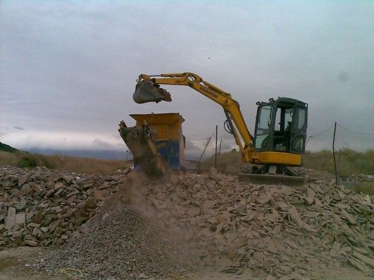 Excavadora amarilla descargando escombros en un camión en una obra de construcción.