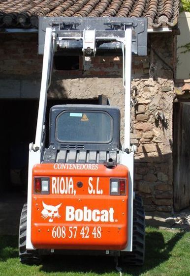 Una minicargadora Bobcat levanta un palé frente a un edificio de piedra.