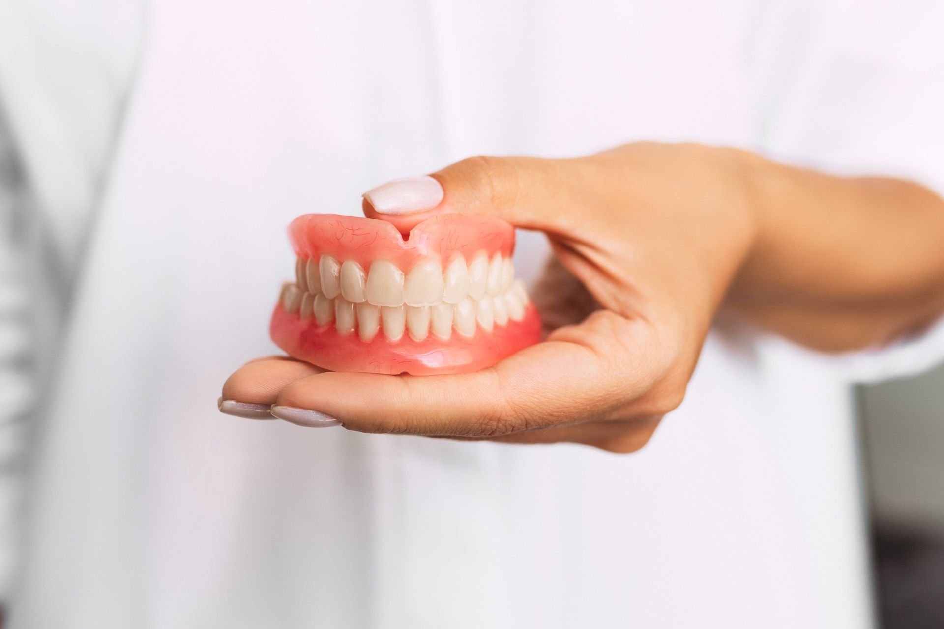Una mujer sostiene un modelo de dentadura postiza en su mano.