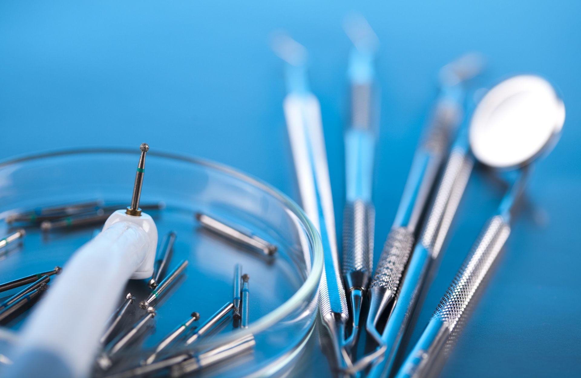 Un primer plano de instrumentos dentales en una placa de Petri sobre un fondo azul.
