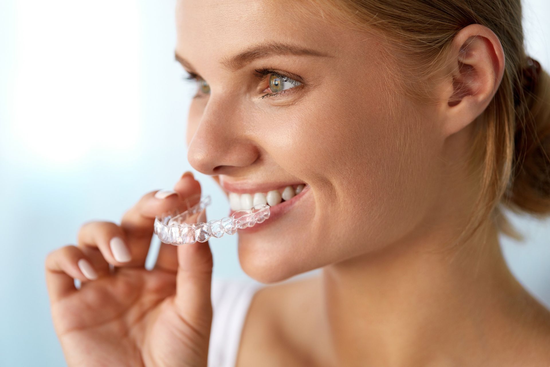 Una mujer sostiene un aparato dental transparente en su boca.