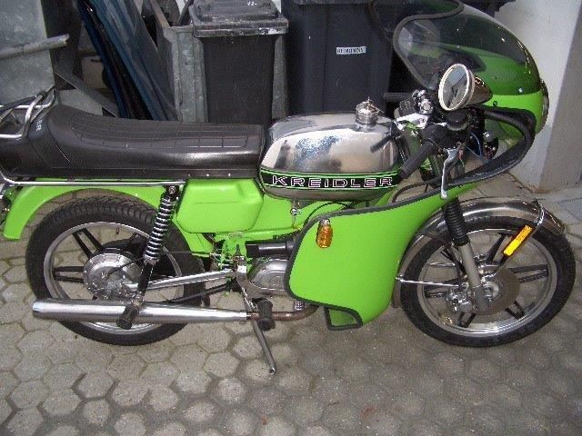 Ein grünes Motorrad steht vor einer schwarzen Mülltonne