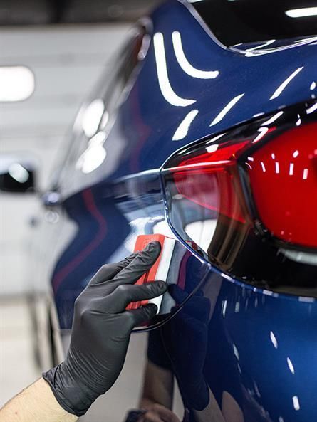 Eine Person mit schwarzen Handschuhen poliert die Rückseite eines blauen Autos.
