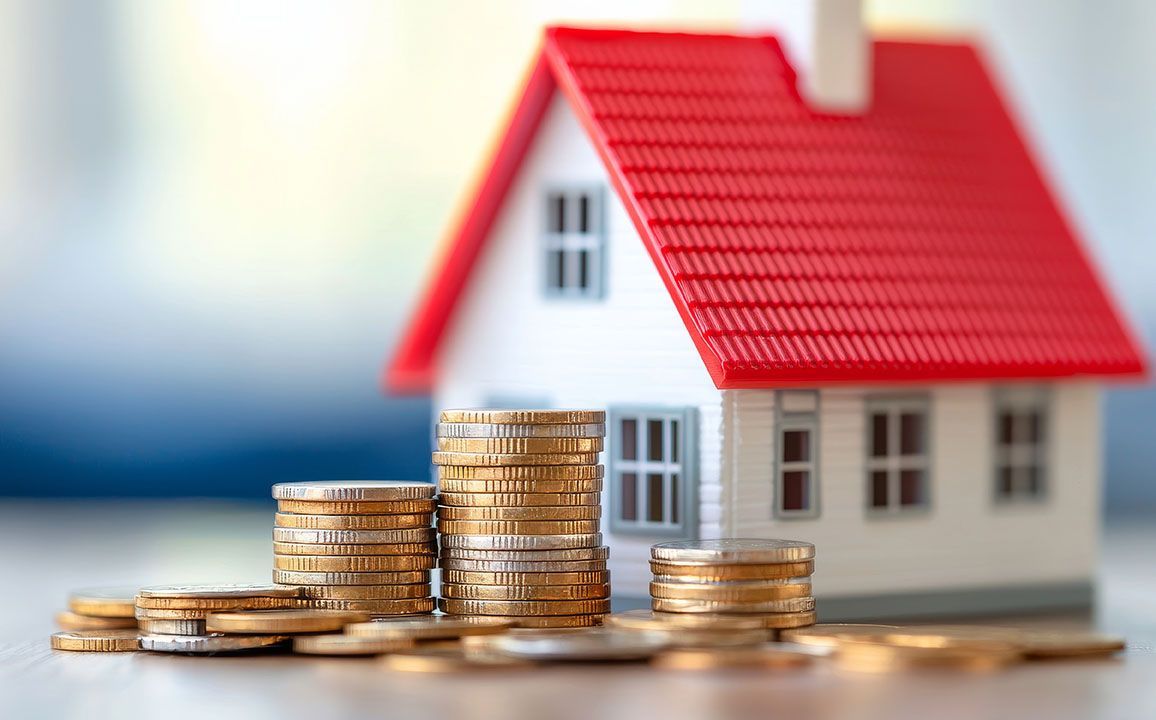 Piles de pièces devant une maquette de maison
