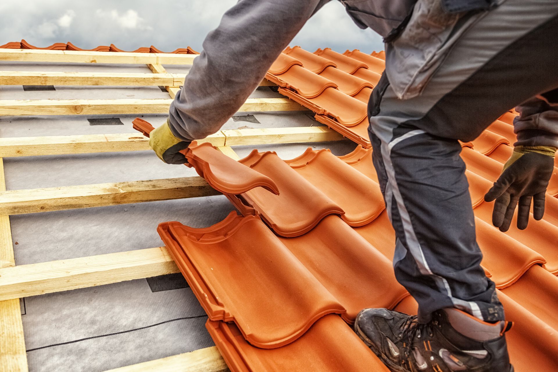 Ouvrier installant des tuiles orange sur un toit en pente