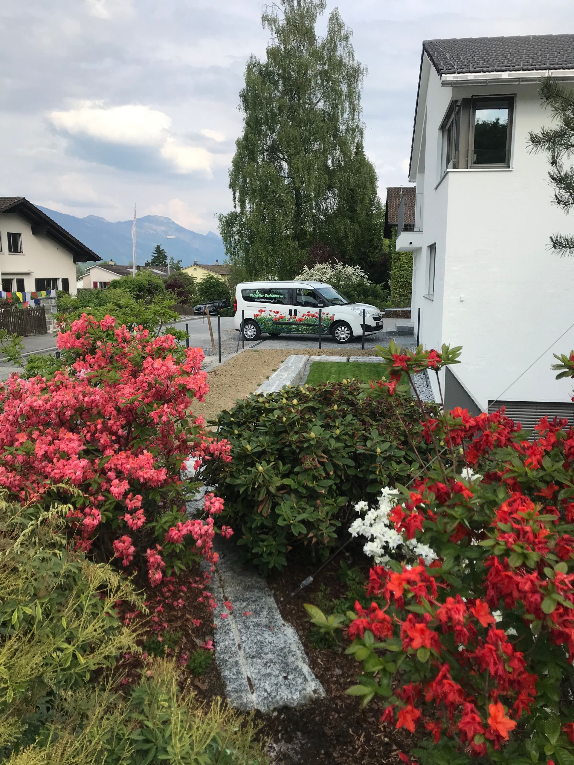 A white van is parked in front of a house surrounded by flowers.