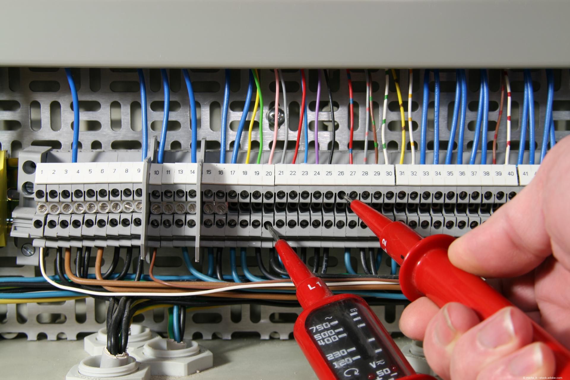 Farbige Kabel formen ein Haus auf einem technischen Bauplan, daneben ein Stromstecker.