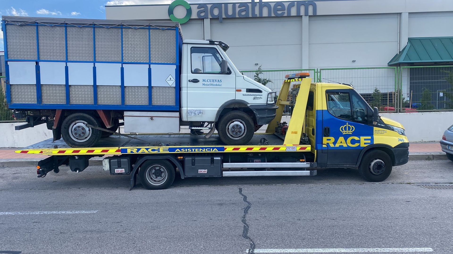 Una grúa azul y amarilla está remolcando un camión blanco.
