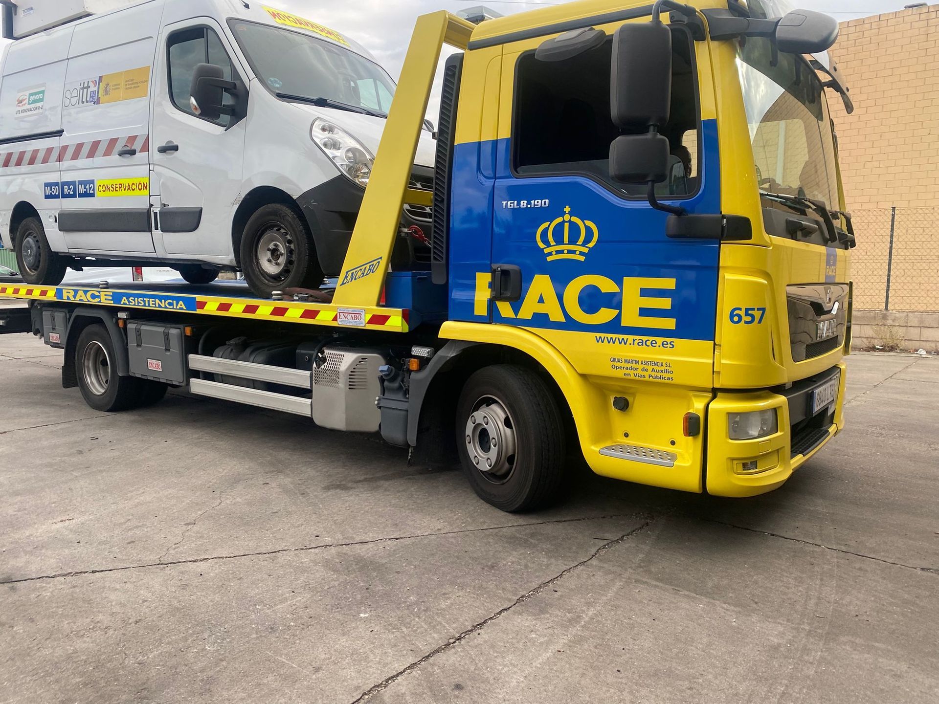 Una grúa de carreras amarilla y azul transporta una camioneta blanca.