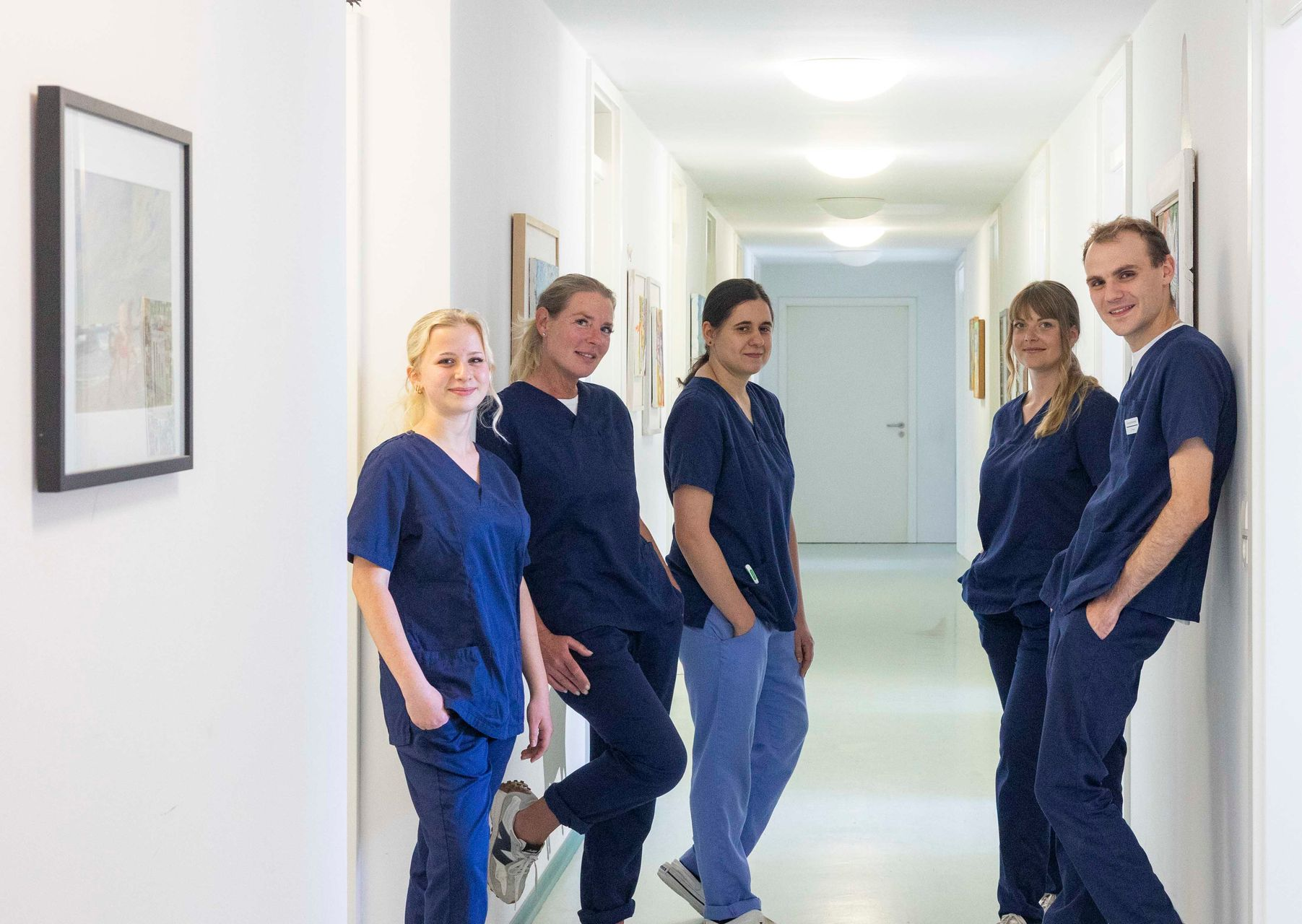 Fünf medizinische Fachkräfte in blauer OP-Kleidung stehen in einem hellen Krankenhausflur.