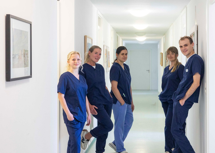 Fünf medizinische Fachkräfte in blauer OP-Kleidung stehen in einem hellen Krankenhausflur.