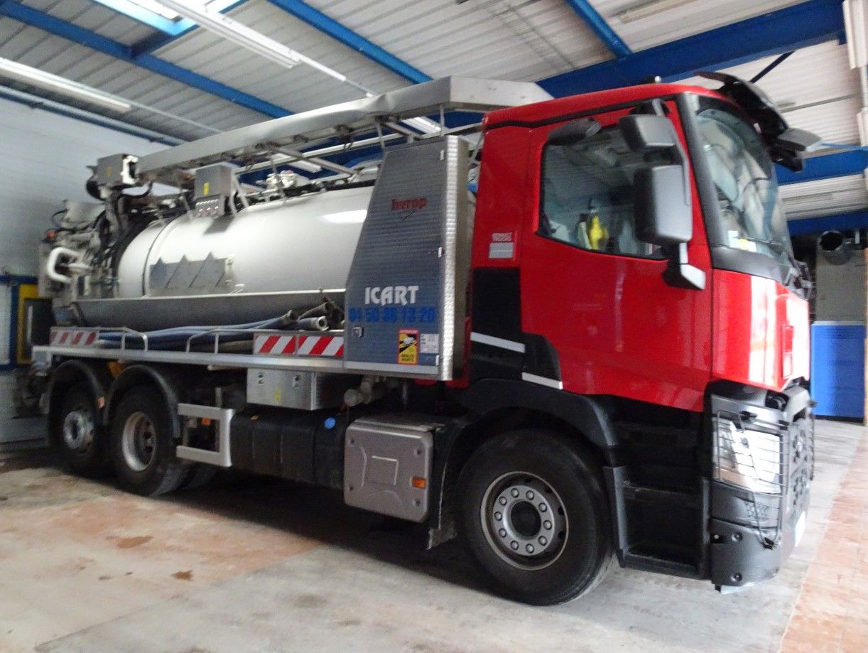 Un camion aspirateur industriel rouge est stationné dans un garage.