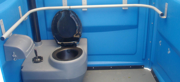 Intérieur d'une cabine de toilettes portables bleues avec un siège de toilette, une base de toilette grise et une barre d'appui de sécurité blanche le long des murs.