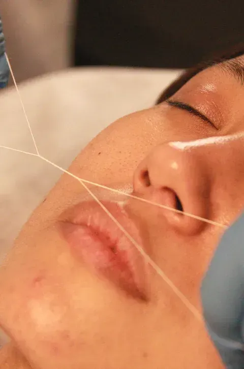 Una mujer se está haciendo un tratamiento de depilación con hilo en la cara.