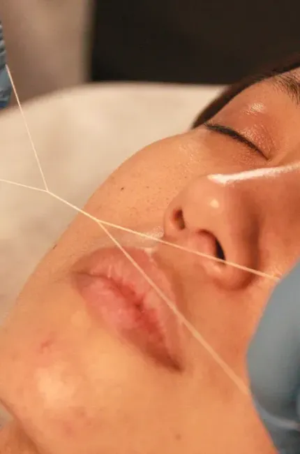 Una mujer se está haciendo un tratamiento de depilación con hilo en la cara.