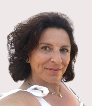 Mujer con cabello oscuro y rizado, con un top blanco y un collar dorado, sonríe a la cámara.