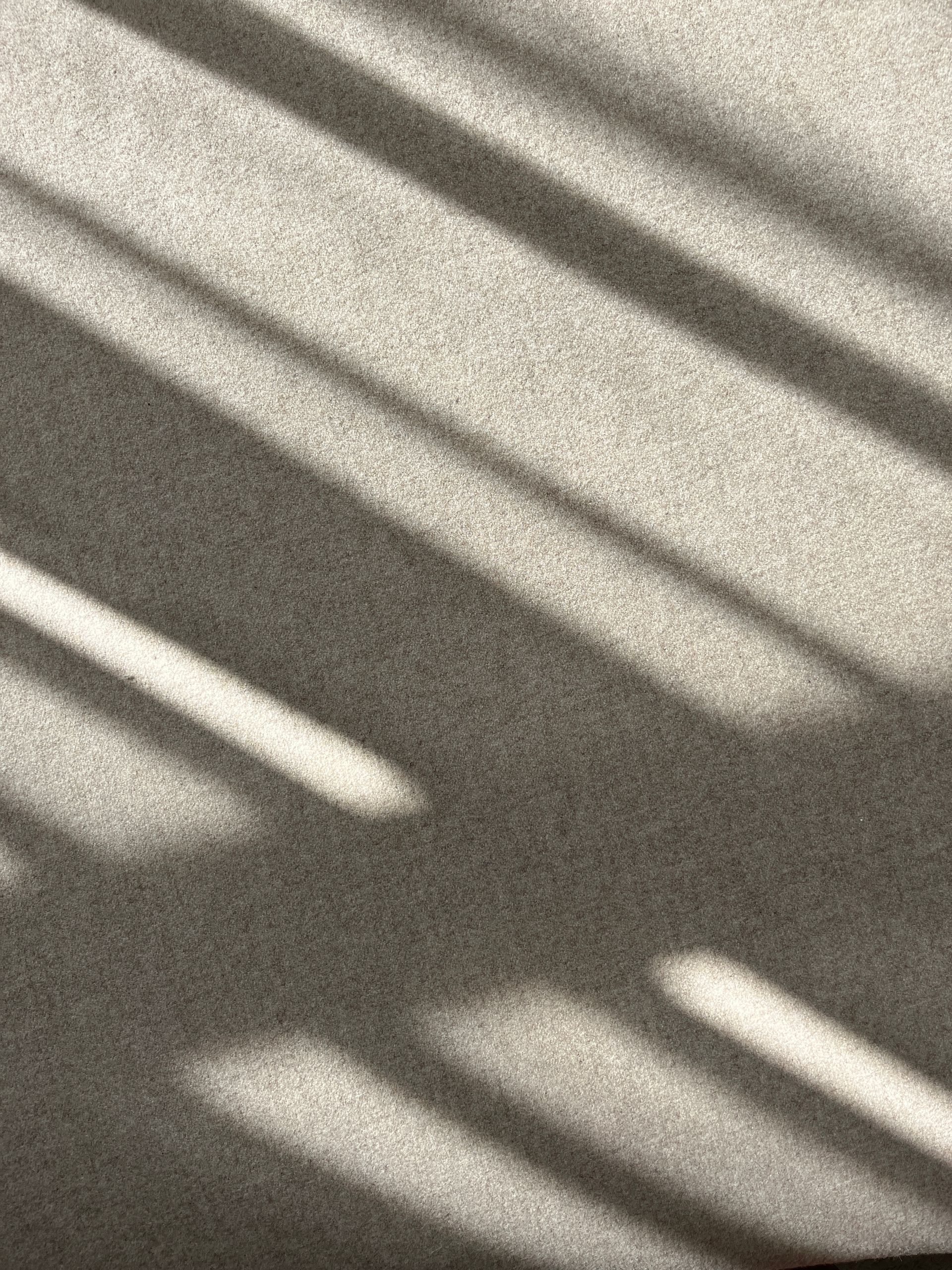 Sombras del marco de una ventana proyectadas sobre una superficie gris clara y texturizada.