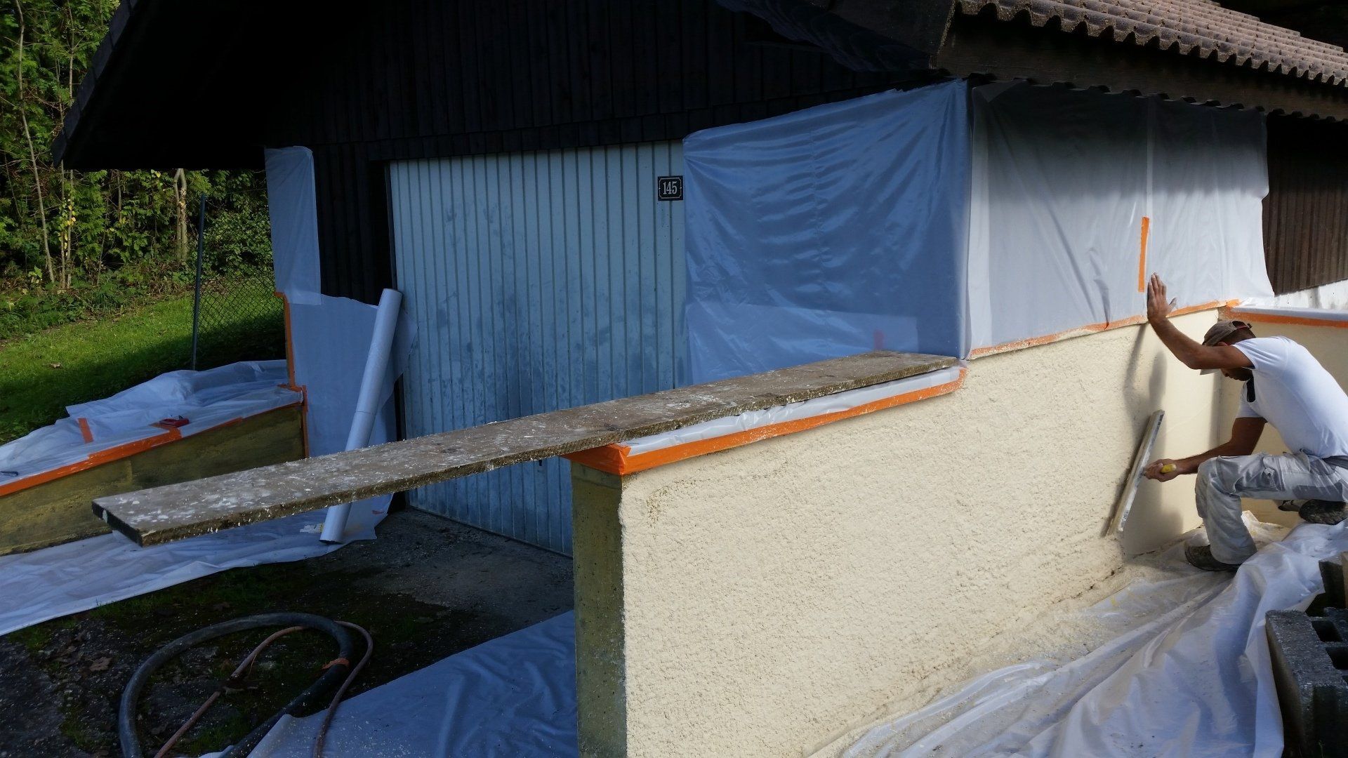 Un ouvrier du bâtiment applique un enduit blanc cassé sur un muret