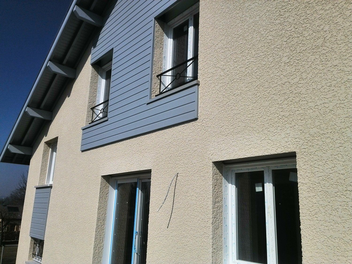 La façade d'une maison avec un enduit texturé et un bardage gris