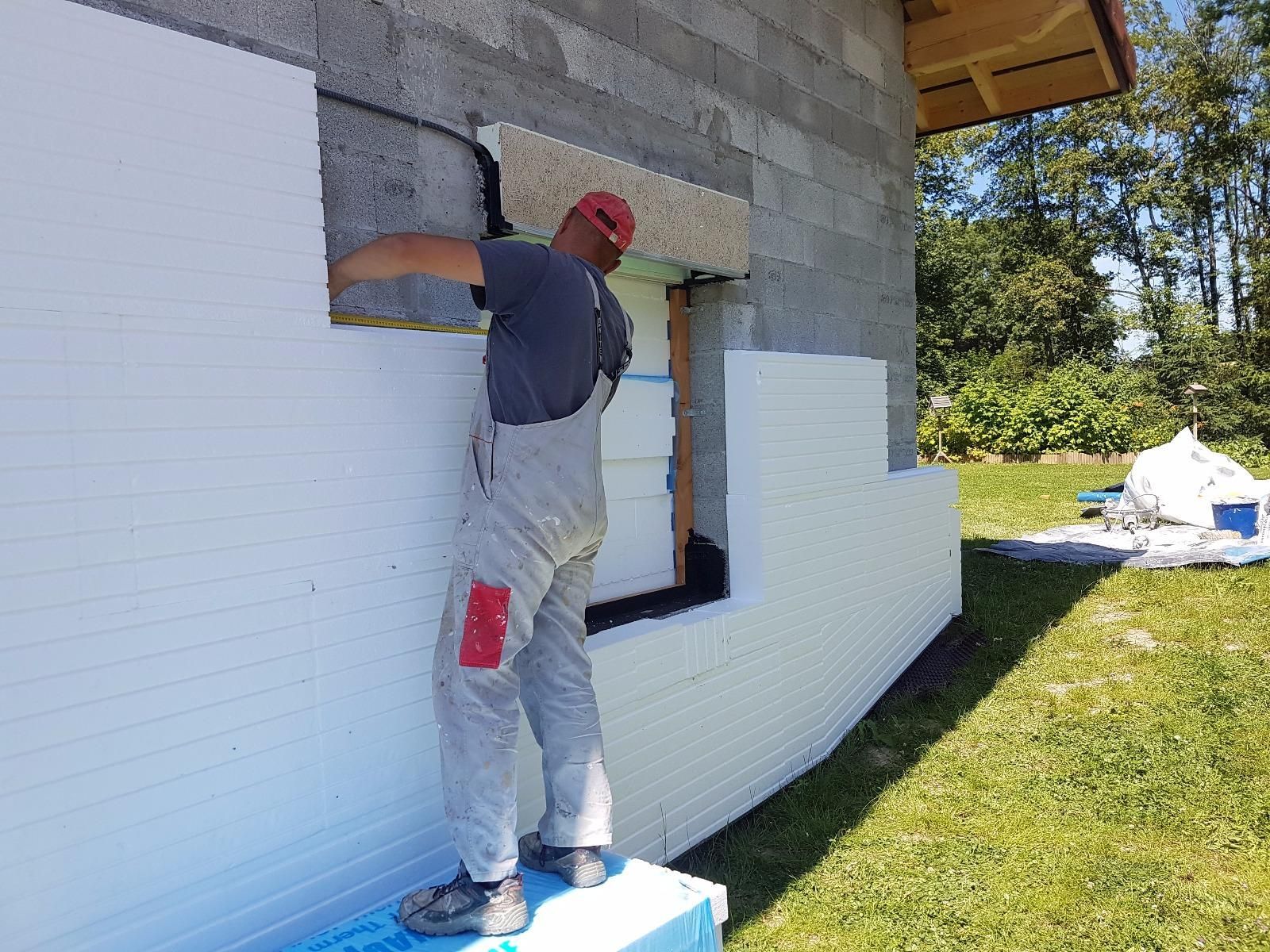 Un ouvrier réalise l'isolation d'une maison en posant un bardage blanc