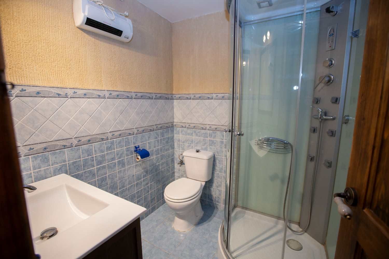 Baño pequeño con lavabo, inodoro y cabina de ducha de cristal con detalles de azulejos azules.