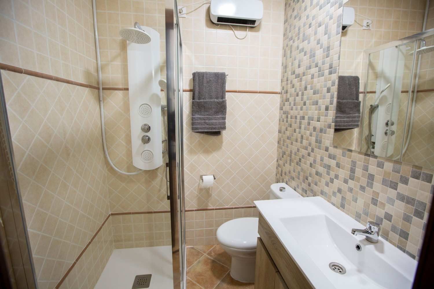 Baño accesible con ducha a ras de suelo, lavabo, inodoro y paredes alicatadas en color beige.