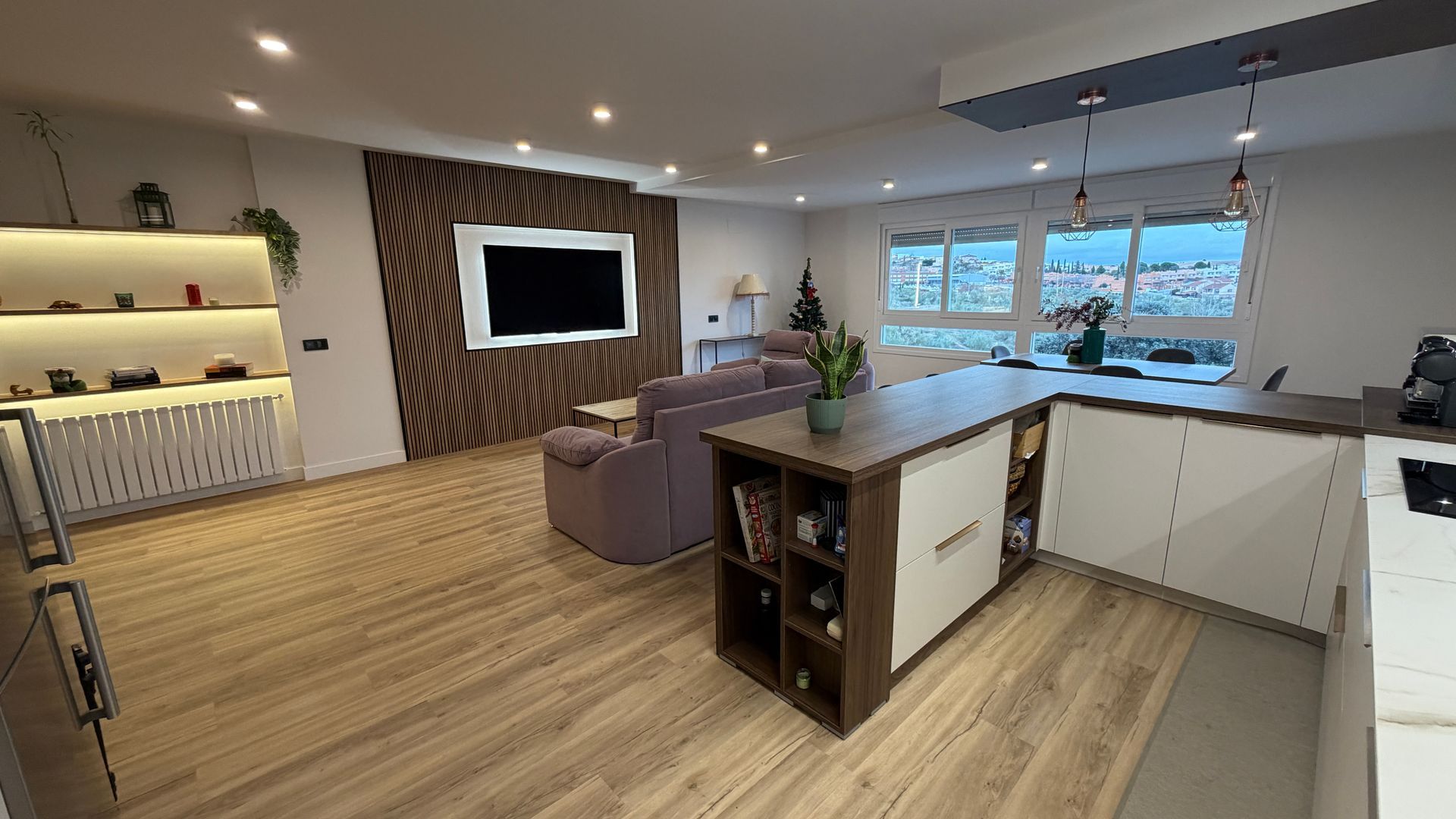 Moderno espacio habitable de planta abierta con isla de cocina, sala de estar con TV y pisos de madera.