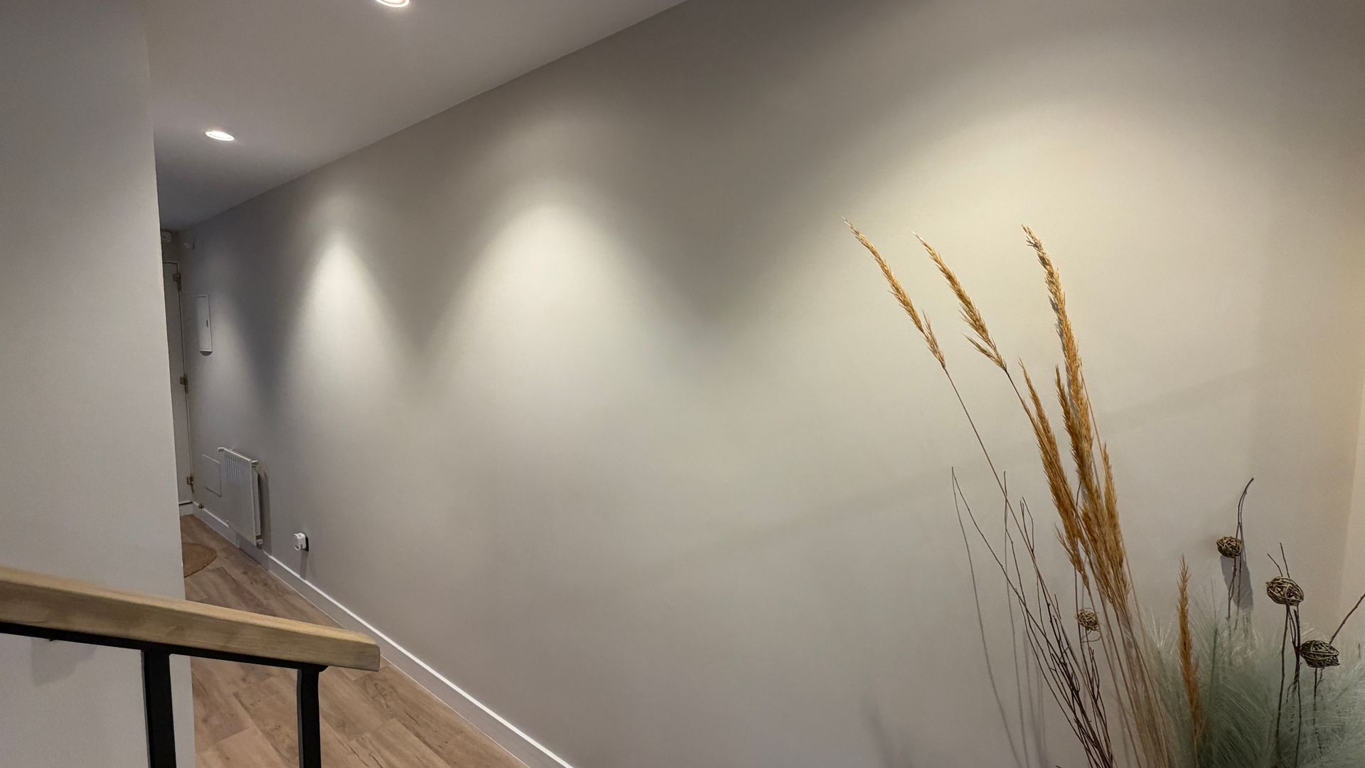 Pasillo con iluminación empotrada, paredes de color gris claro, suelo de madera y hierbas secas decorativas.