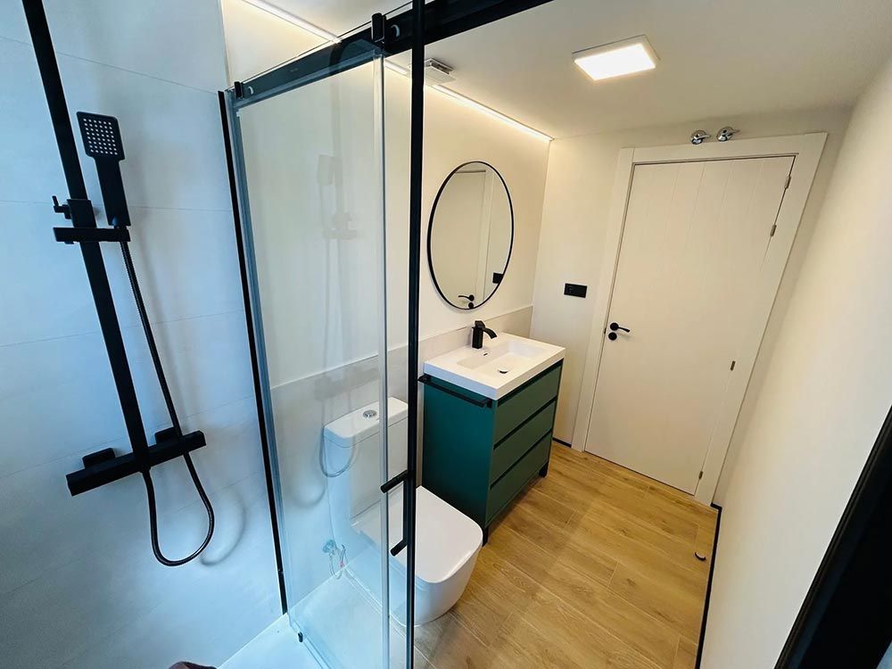 Baño moderno con accesorios de ducha negros, tocador verde y puerta blanca.