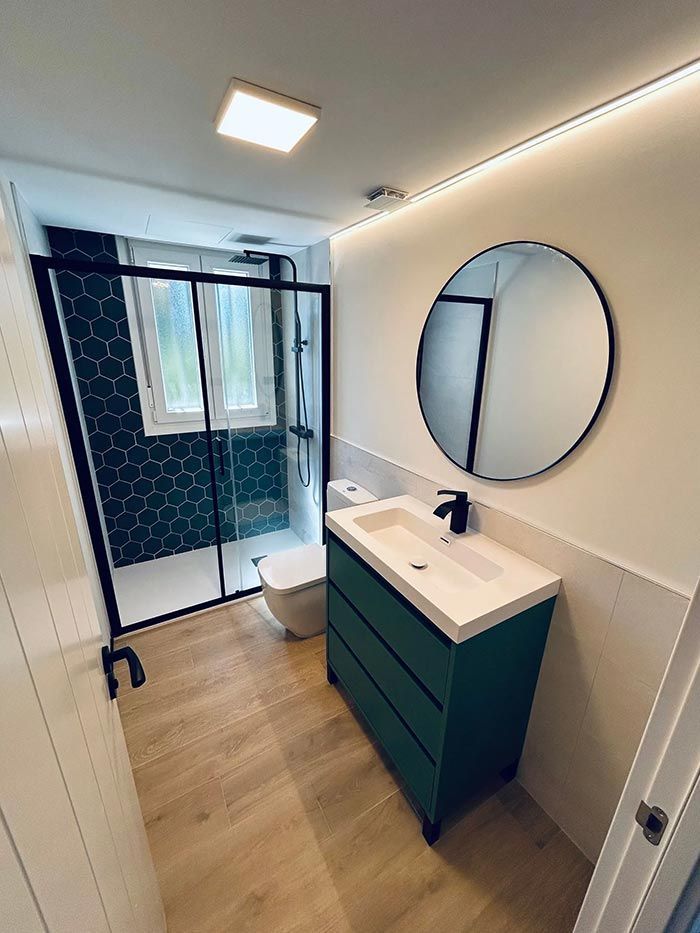 Baño verde y blanco con ducha, tocador, inodoro y espejo redondo.