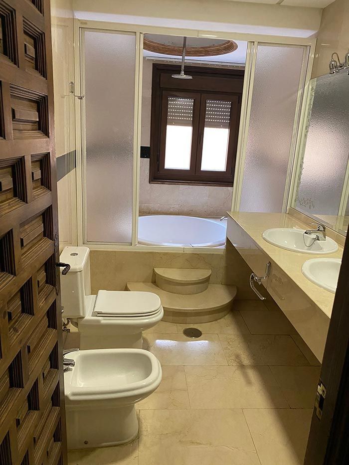 Baño con inodoro, bidé, lavabo doble y bañera hundida detrás de un vidrio esmerilado.