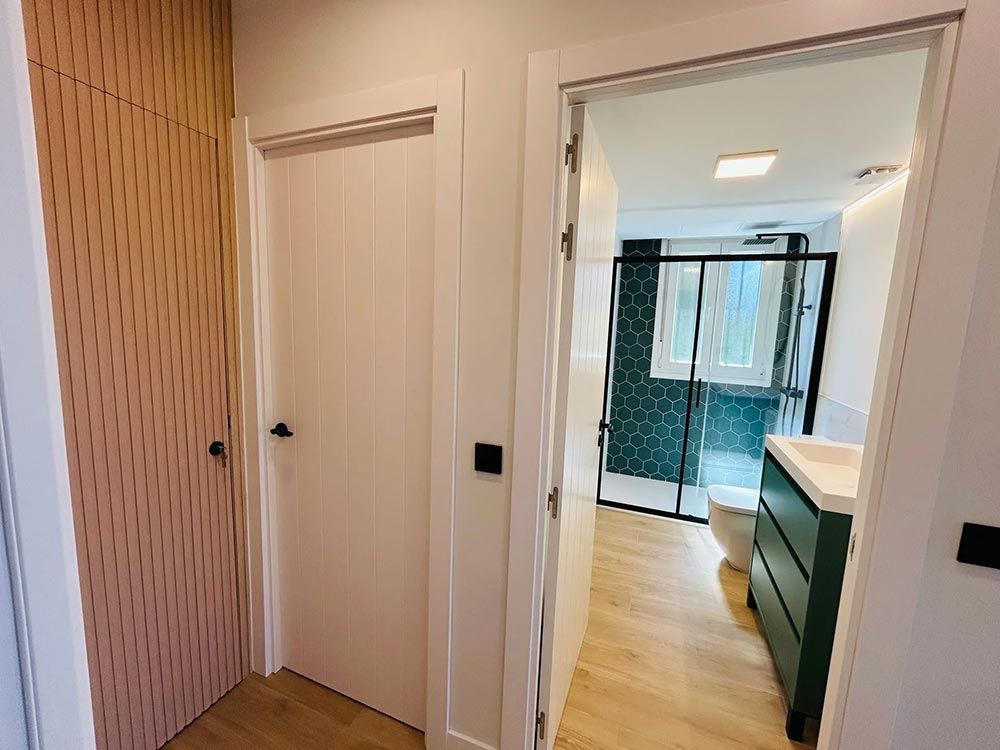 Pasillo con puerta de armario de madera, puerta blanca y puerta abierta a baño.