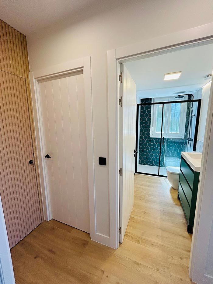 Pasillo con puerta a un baño con tocador verde, mampara de ducha negra y armario de madera a la izquierda.