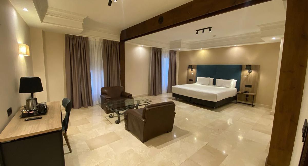 Habitación de hotel con cama grande, zona de estar, escritorio y suelos de mármol.