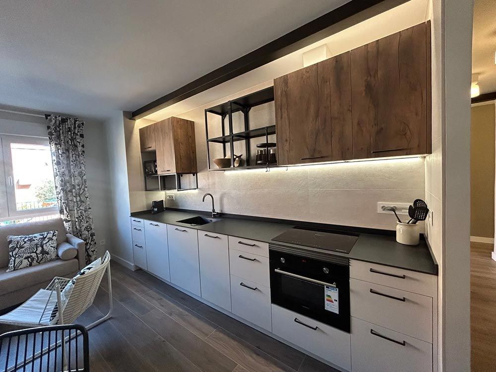 Cocina moderna con gabinetes claros, encimeras oscuras y gabinetes superiores en tonos madera.