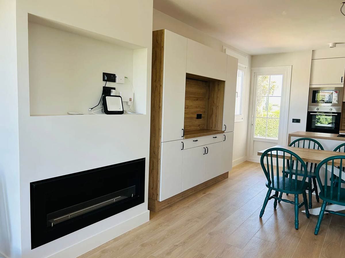 Interior con chimenea, gabinetes empotrados y comedor con mesa redonda y sillas color verde azulado.