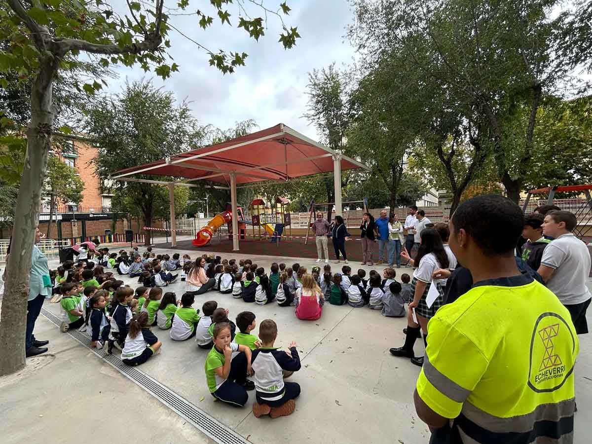 Niños sentados en círculo escuchando a un orador en un parque con zona de juegos.